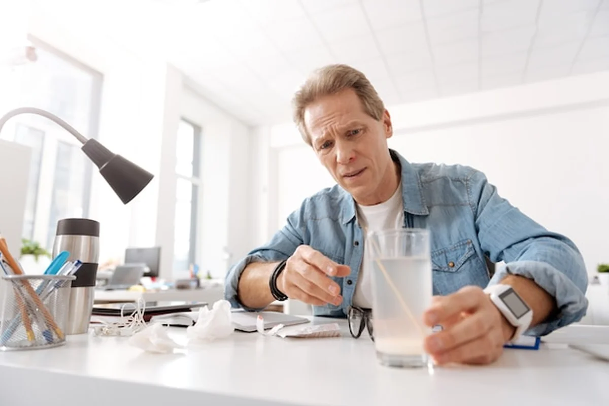 Chory mężczyzna siedzi przy stole, marszcząc czoło, patrząc na lek