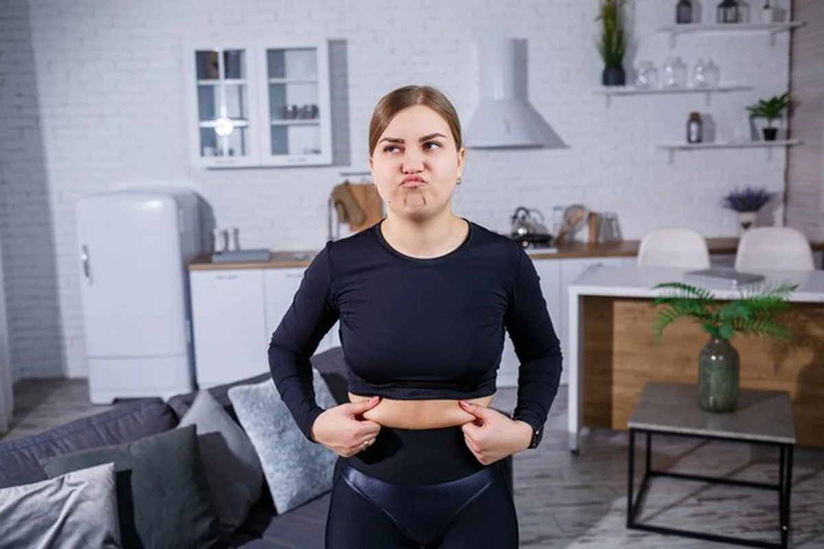 Młoda kobieta w legginsach pokazuje fałdę na brzuchu, uprawiając sport w domu