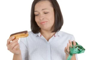 Młoda kobieta wybierająca między czekoladowym eklerem a zdrowiem na białym tle