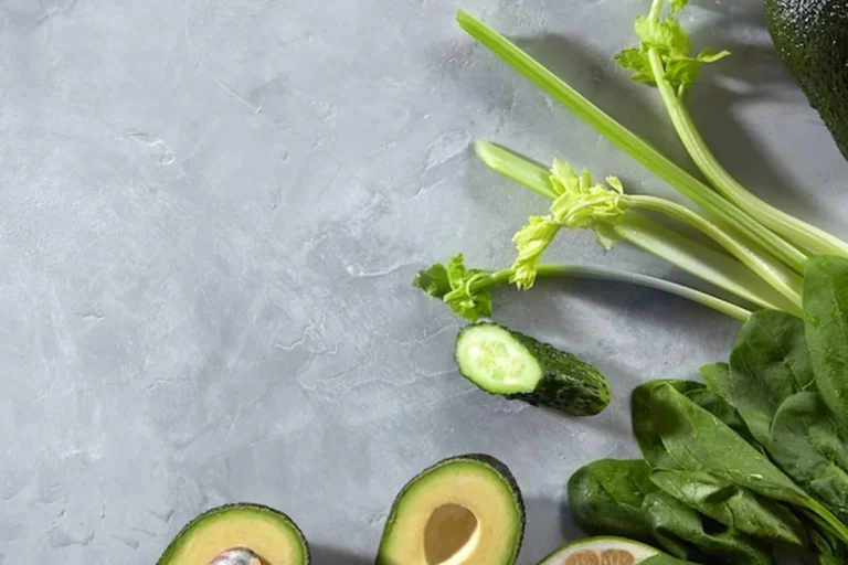 Świeże warzywa na szarej ścianie: szpinak, ogórek, limonka, seler, awokado, idealne do sałatek i smoothie