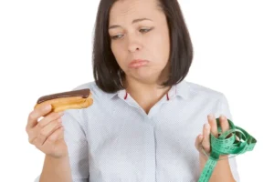 Młoda kobieta wybierająca między czekoladowym eklerem a zdrowiem na białym tle