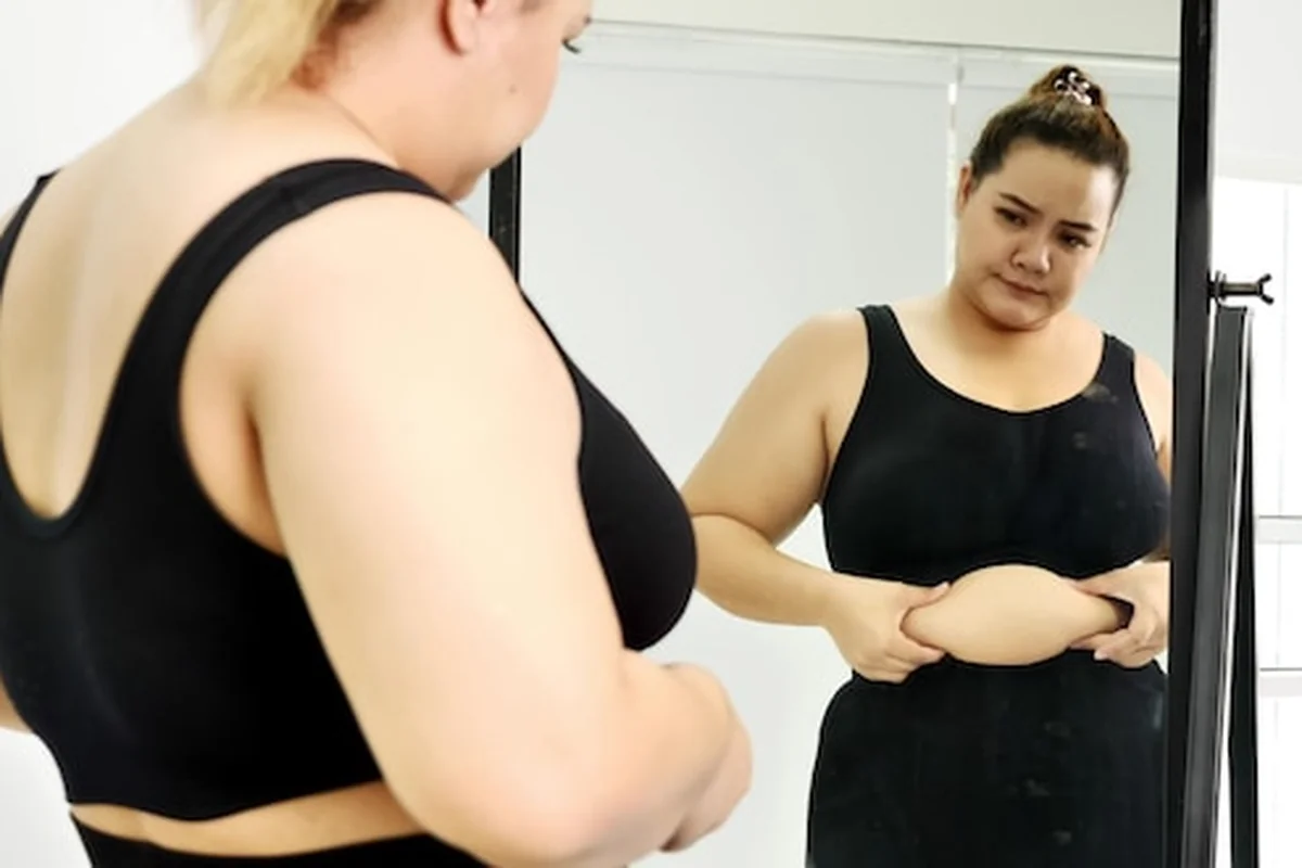 Gruba kobieta patrzy na swój brzuch w lustrze