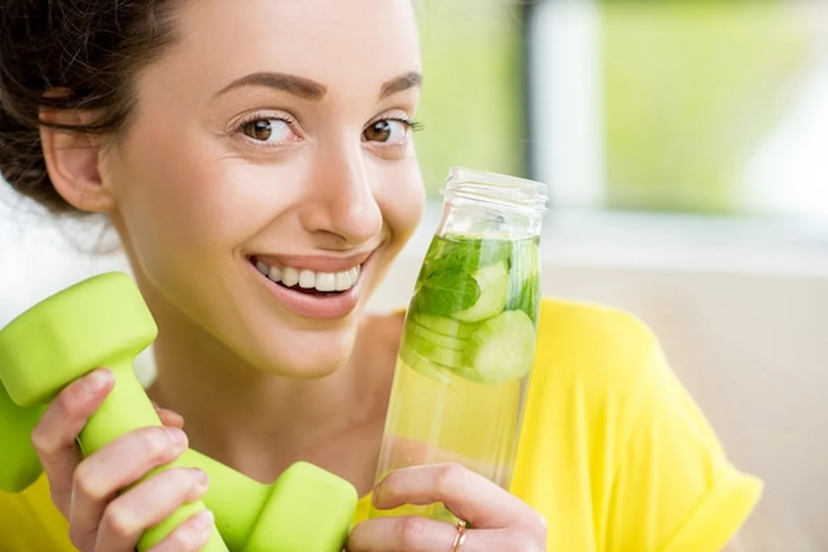 Kobieta pije wodę z miętą, ogórkiem i limonką podczas treningu z hantlami